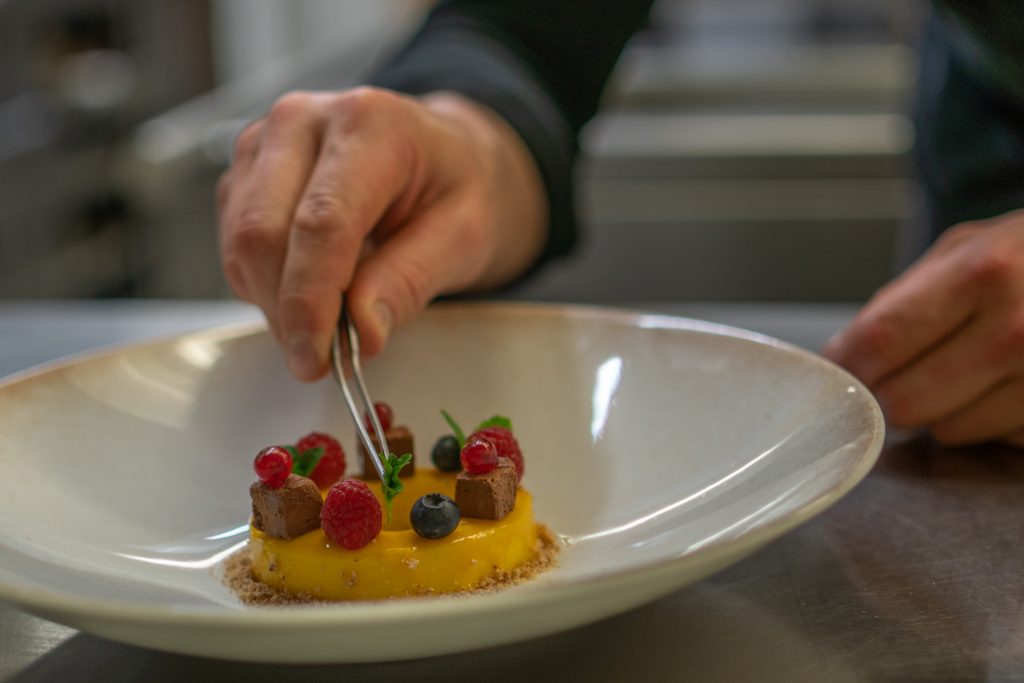 Teller mit Dessert, Hand mit Pinzette fügt Minze hinzu