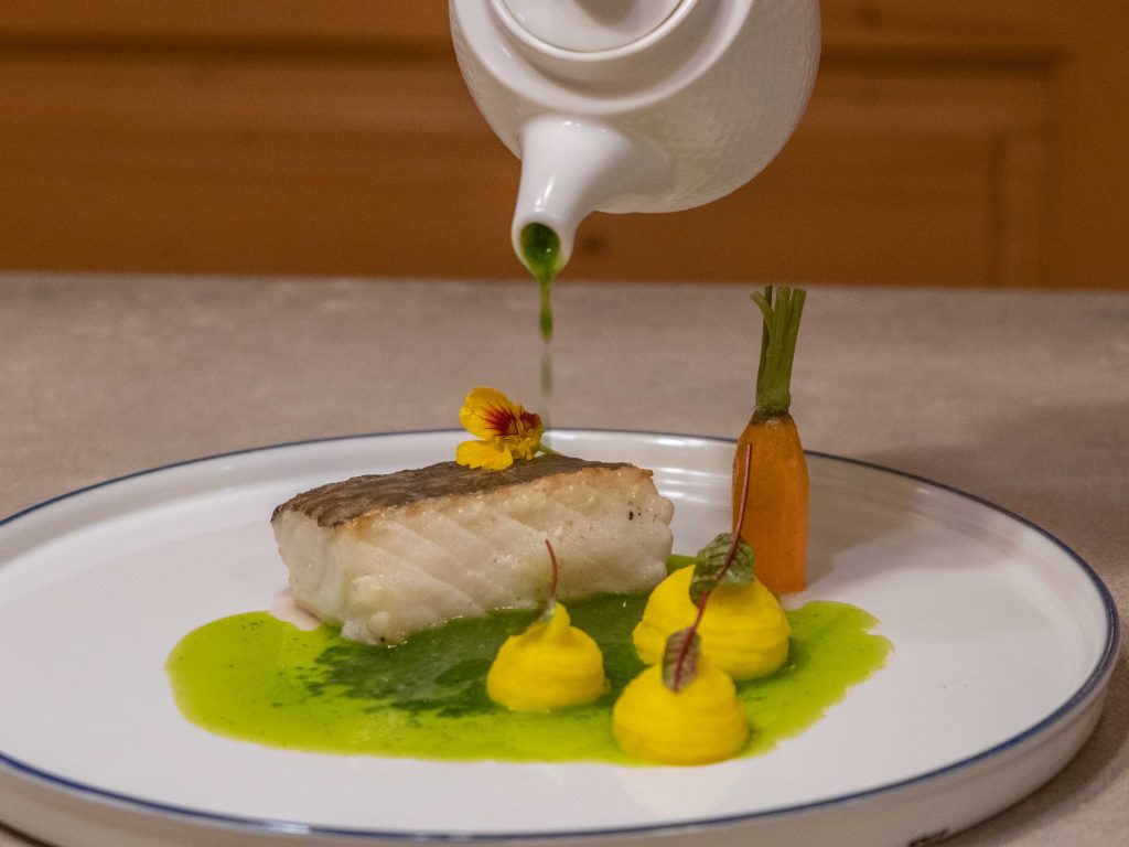 Teller mit gebratenem Fisch und Soße wird aus Kännchen übergossen