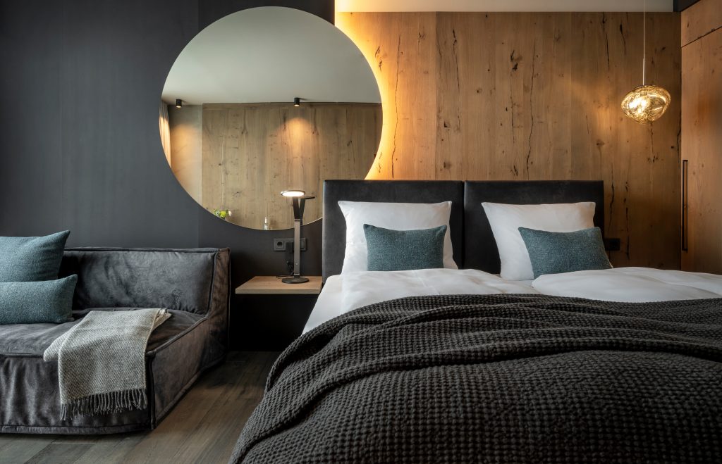 Hotelzimmer mit Bett links davon Sofa und Spiegel an der Wand