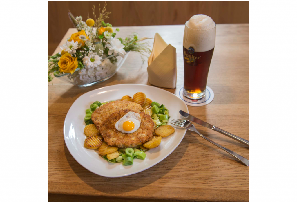 Ein Teller mit Schnitzel, Bratkartoffeln und Gemüse sowie ein dunkles Bier
