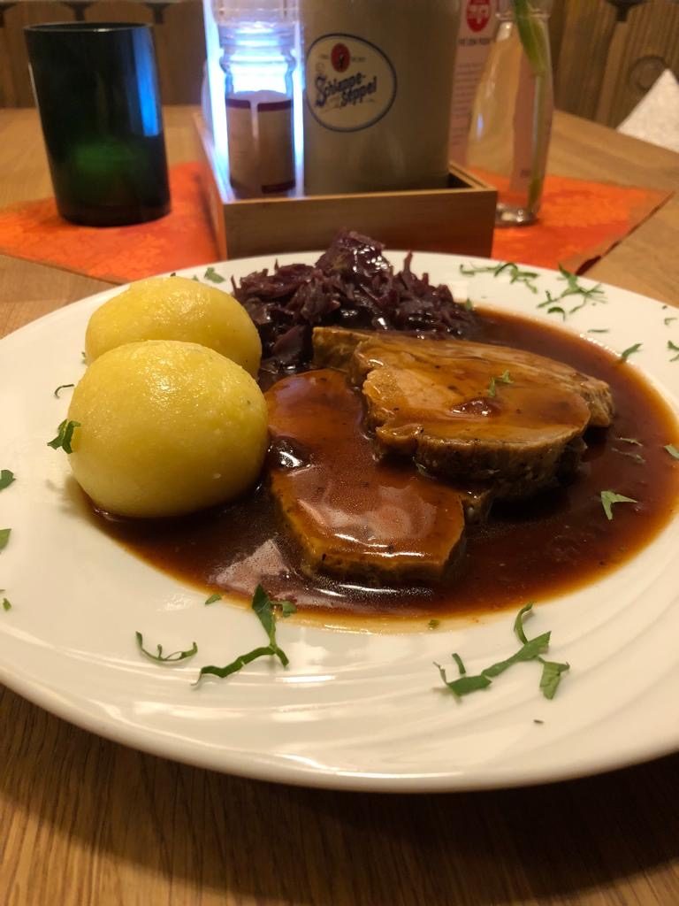 Fleischstücke mit Rotkohl, Knödel und Bratensoße auf einem Teller