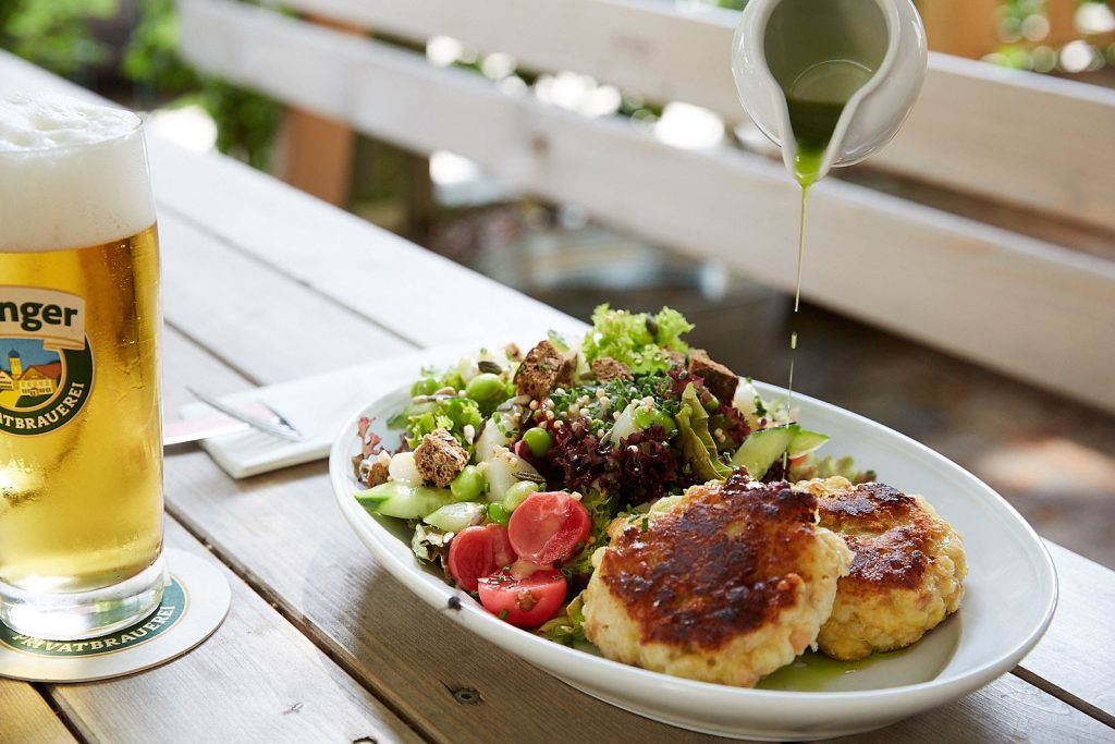 Teller mit zwei kaspressknödeln und Salat Links daneben ein Ayinger Bier im Glas