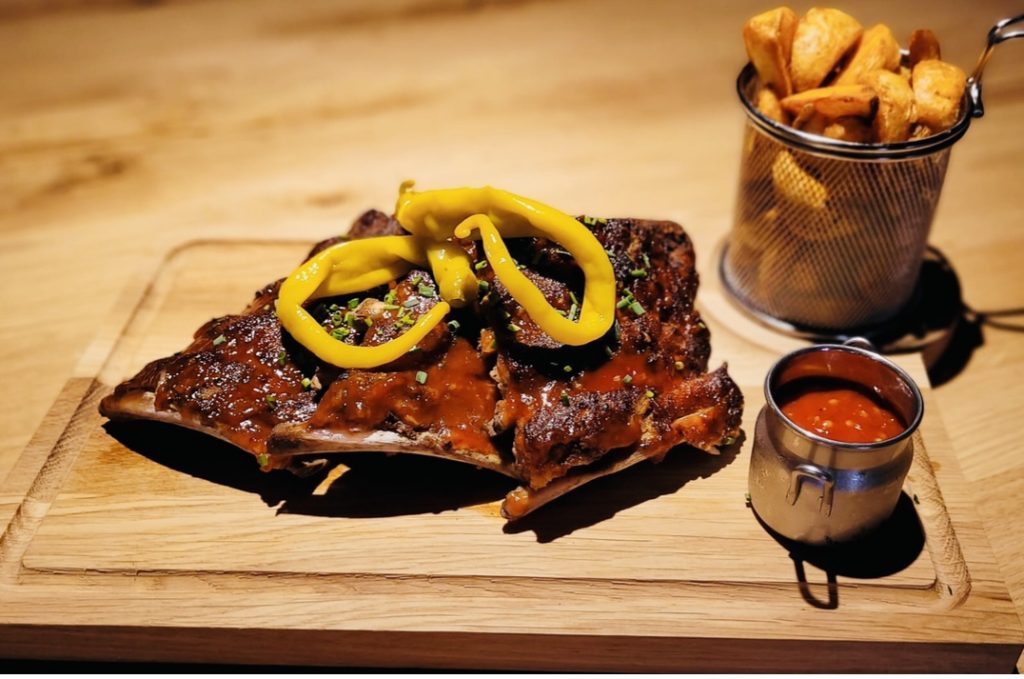 Spareribs Brett mit Peperoni und Kartoffelecken rechts davon.