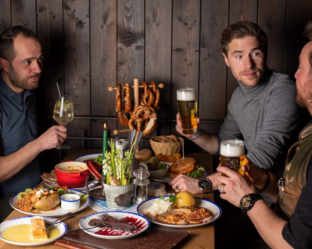 Tisch mit diversen Speisen und 3 Personen mit Getränken in der Hand