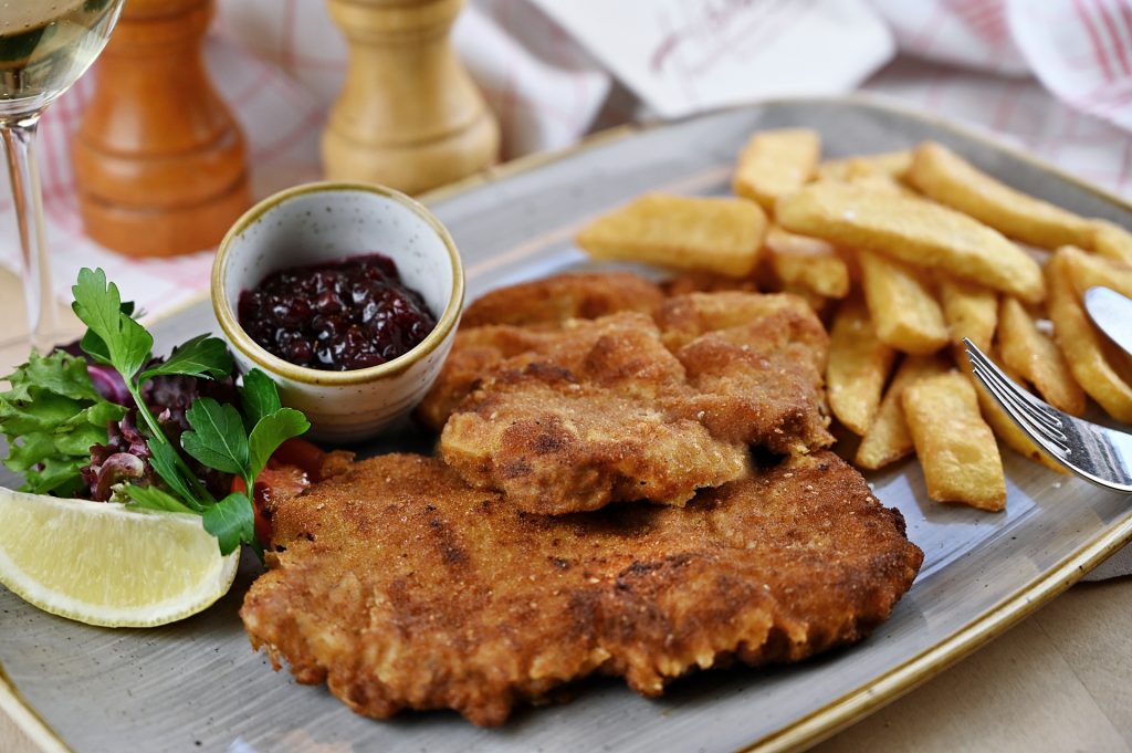 Schnitzel vom Kalbsrücken in Butterschmalz aus der Pfanne gebacken, Steakhousepommes, dazu Preiselbeeren