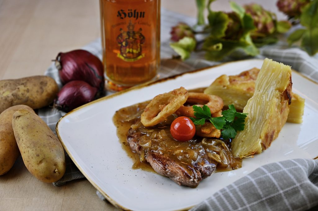 Angus Rinderhüfte mit gebräunten Butterzwiebeln in Görchlabiersoße, dazu gebackene Bierzwiebelringe und hausgemachtes Kartoffelgratin