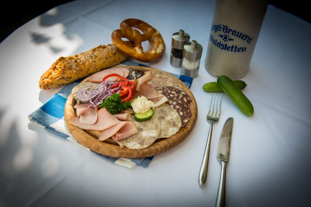 Brauerei Engel Brotzeit auf Holzbrett mit Bierkrug und Menagen im Hintergrund