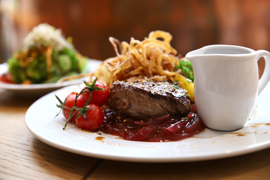 Zwiebelrostbraten auf glasierten Zwiebeln mit Tomaten und Soße im Kännchen