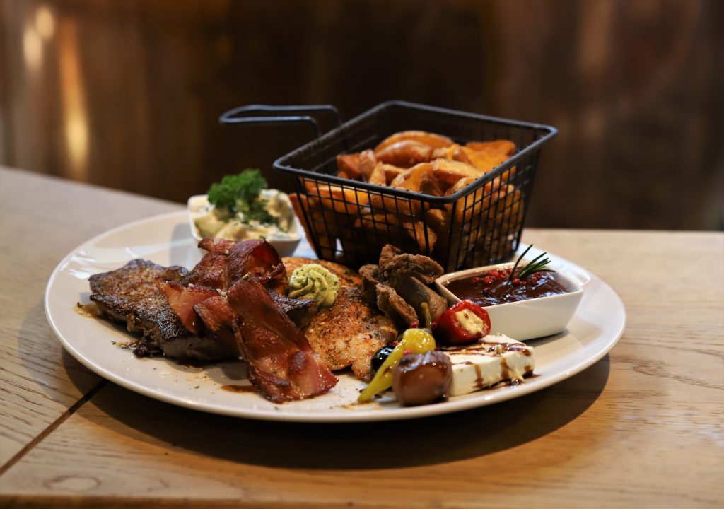 Grillteller mit Kartoffelwedges im Körbchen und Soßen