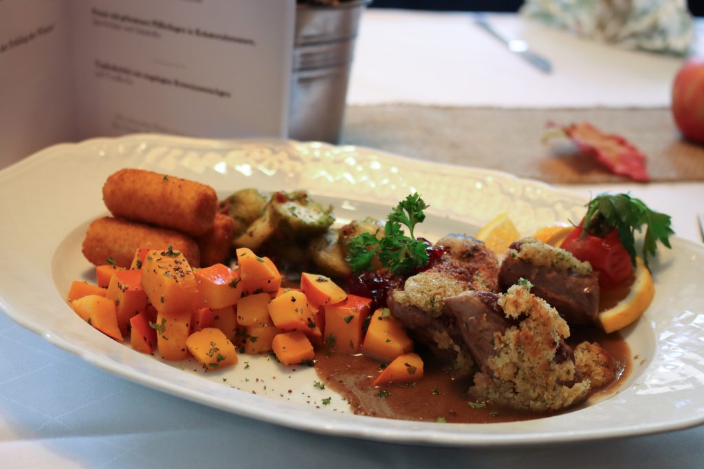Fleischgericht auf Teller mit Kroketten und Kürbis