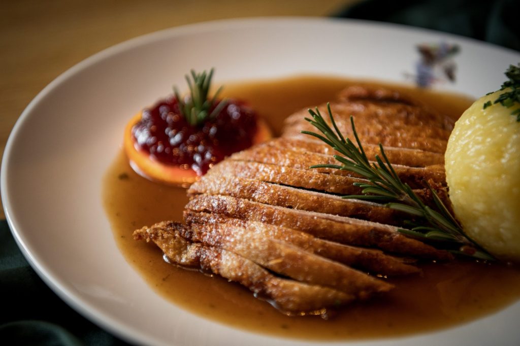 Entenbrust geschnitten auf einem Teller mit Kartoffelknödel und Preiselbeeren in Soße