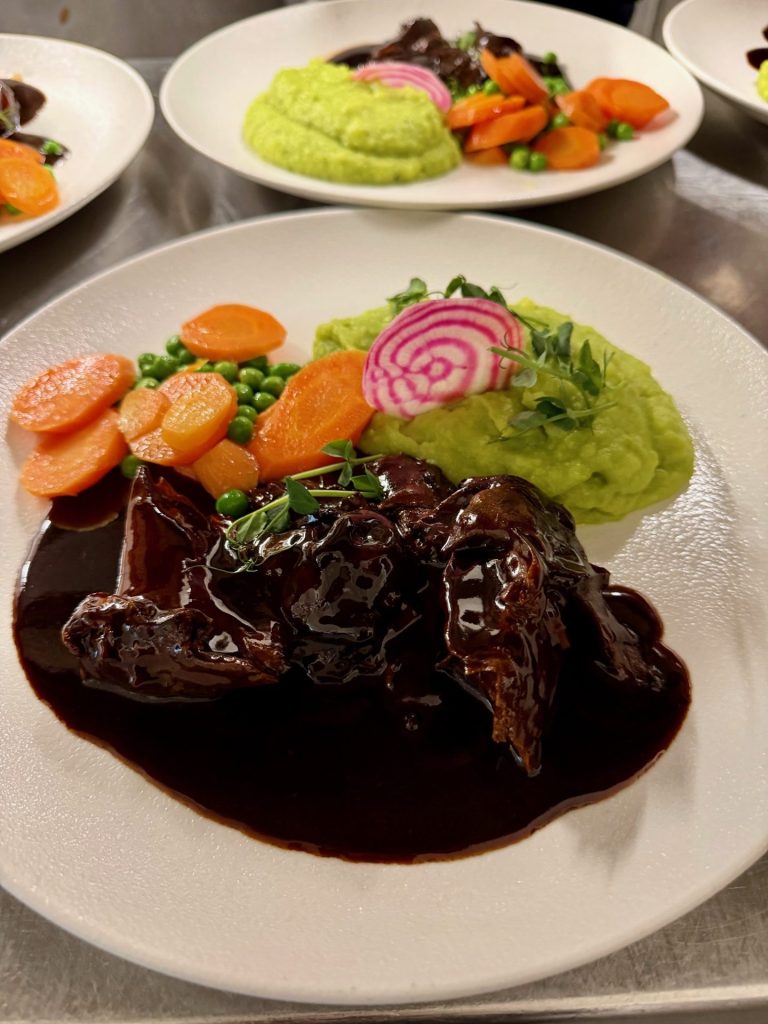 Braten mit dunkler Soße und Erbesnpürre auf Teller mit Karottengemüse