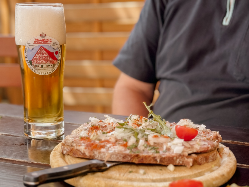 links im Bild Bier, mittig Holzbrett mit Griebenschmalz und Zwiebeln auf Graubrot. Dahinter sitzt ein Gast.