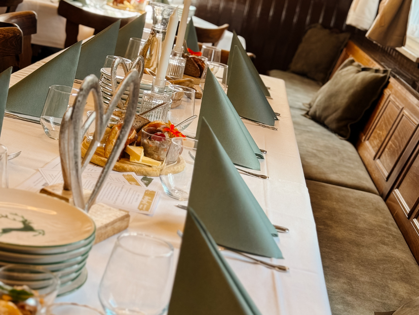 eingedeckter Tisch mit weißer Tischdecke und grünen Servitetten. rechts sind die bräunlich gepolsterten Bänke zu sehen.