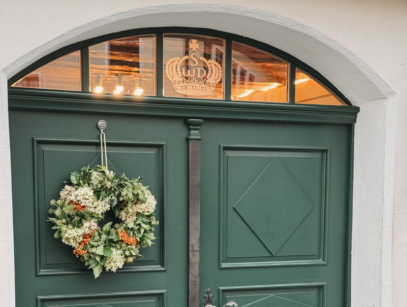 Grüne zweiflüglige Eingangstür mit Blumenkranz links