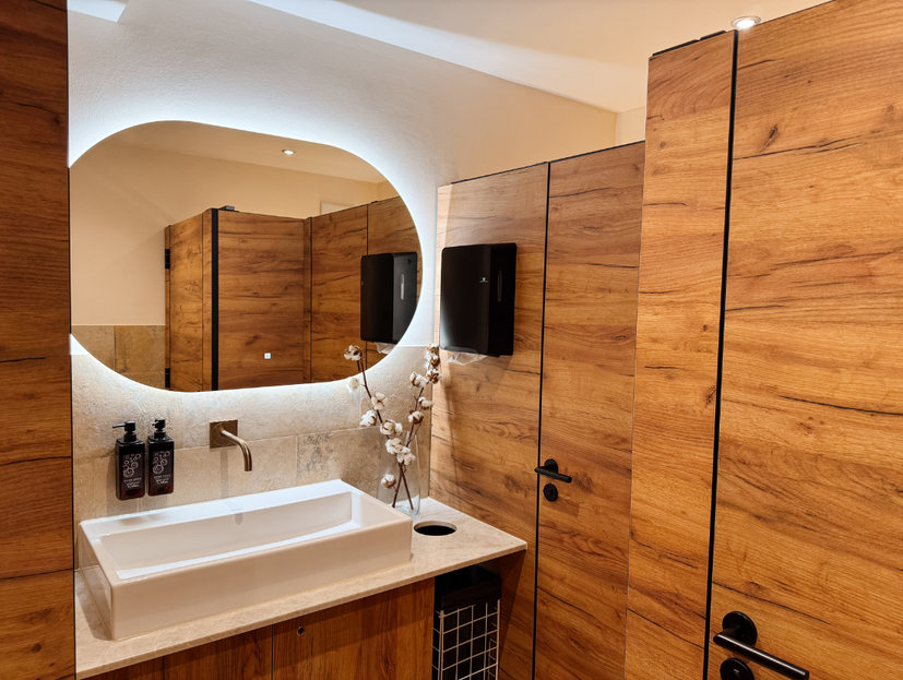 Aufnahme des Badezimmers mit ovalem Spiegel, weißen Armaturen und Holzmöbeln.