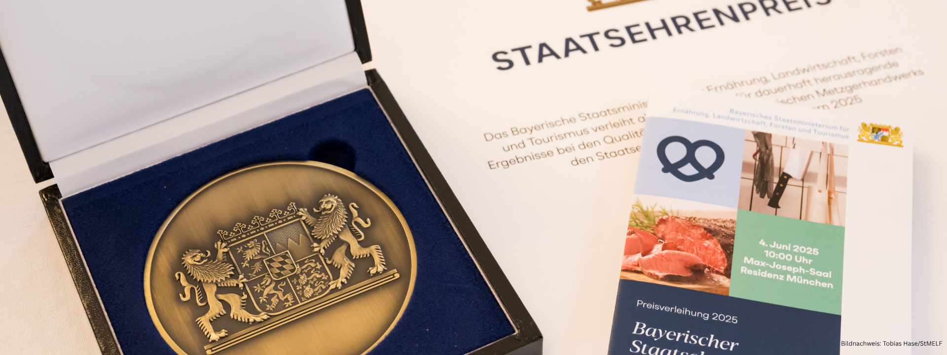 Links Plakette mit Staatswappen und rechts Auschnitt Urkunde des Staatsehrenpreise sowie oben aufliegend Flyer der Veranstaltung am 4. Juni 25